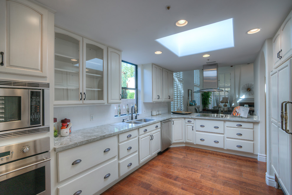 Photo of a mid-sized arts and crafts l-shaped eat-in kitchen with a drop-in sink, beige cabinets, marble benchtops, white splashback, subway tile splashback, stainless steel appliances and medium hardwood floors.