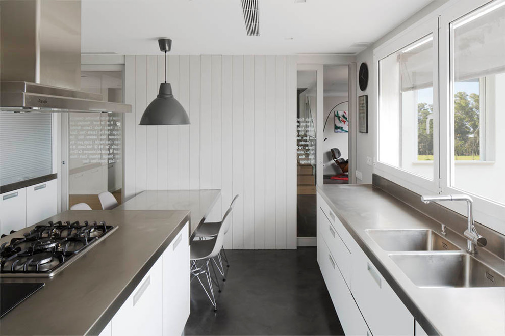 Inspiration for a large scandinavian galley separate kitchen in Barcelona with a double-bowl sink, flat-panel cabinets, white cabinets, stainless steel benchtops, stainless steel appliances, concrete floors, with island and grey benchtop.