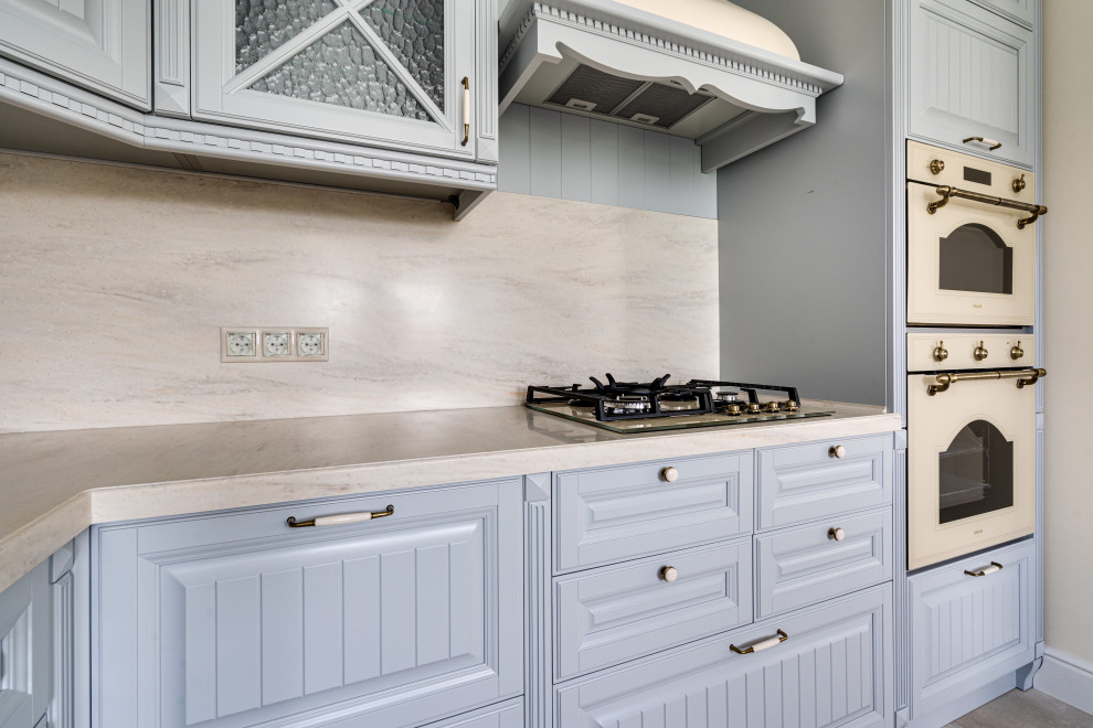 Example of a mid-sized cottage l-shaped porcelain tile and beige floor eat-in kitchen design in Moscow with an integrated sink, raised-panel cabinets, gray cabinets, solid surface countertops, beige backsplash, marble backsplash and beige countertops