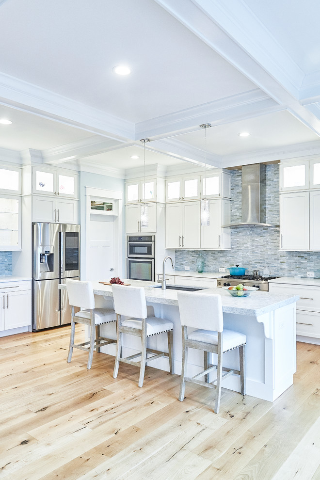 Open concept kitchen - large transitional l-shaped light wood floor and beige floor open concept kitchen idea with an undermount sink, shaker cabinets, white cabinets, blue backsplash, matchstick tile backsplash, stainless steel appliances, an island and white countertops