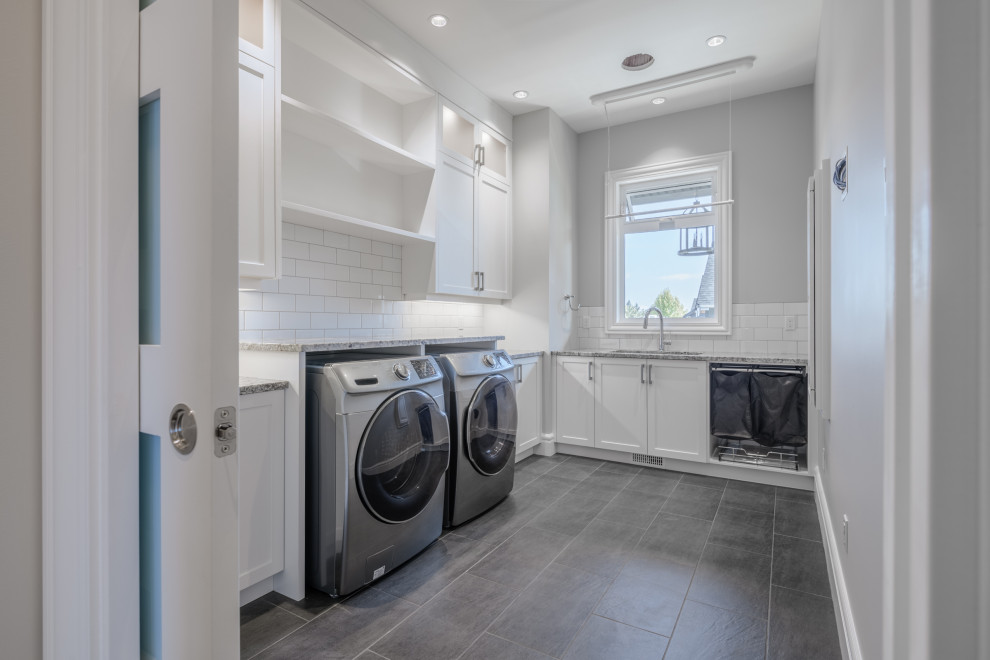 Mid-sized contemporary l-shaped dedicated laundry room in Other with an undermount sink, recessed-panel cabinets, white cabinets, granite benchtops, grey walls, slate floors, a side-by-side washer and dryer, grey floor and multi-coloured benchtop.