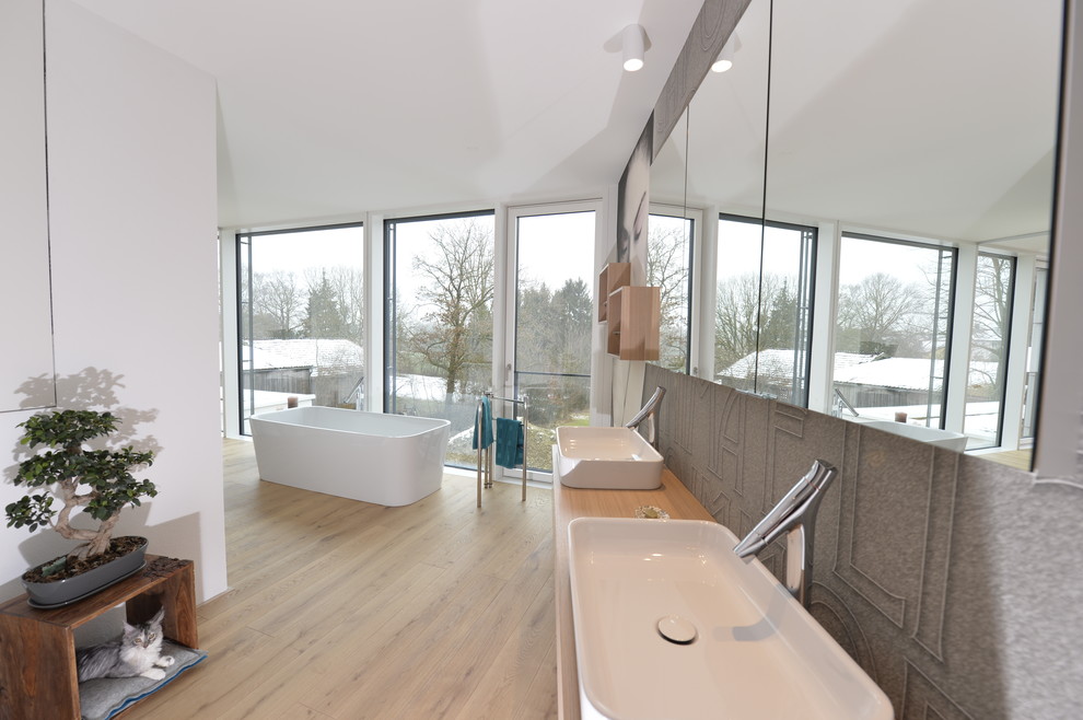 This is an example of an expansive asian master bathroom in Munich with flat-panel cabinets, light wood cabinets, a freestanding tub, a curbless shower, white walls, light hardwood floors, a vessel sink, brown floor and an open shower.
