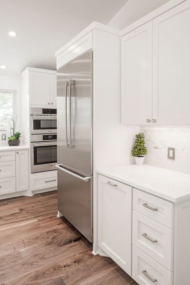 Transitional u-shaped medium tone wood floor enclosed kitchen photo in Austin with shaker cabinets, white cabinets, quartz countertops, white backsplash, stone tile backsplash, stainless steel appliances and a peninsula