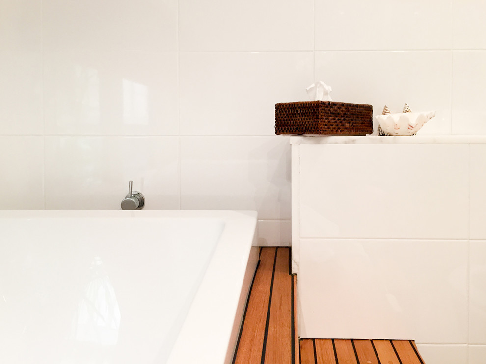 Photo of a mid-sized beach style master bathroom in Sydney with an integrated sink, flat-panel cabinets, white cabinets, marble benchtops, an alcove tub, an alcove shower, a wall-mount toilet, white tile, ceramic tile, white walls and ceramic floors.