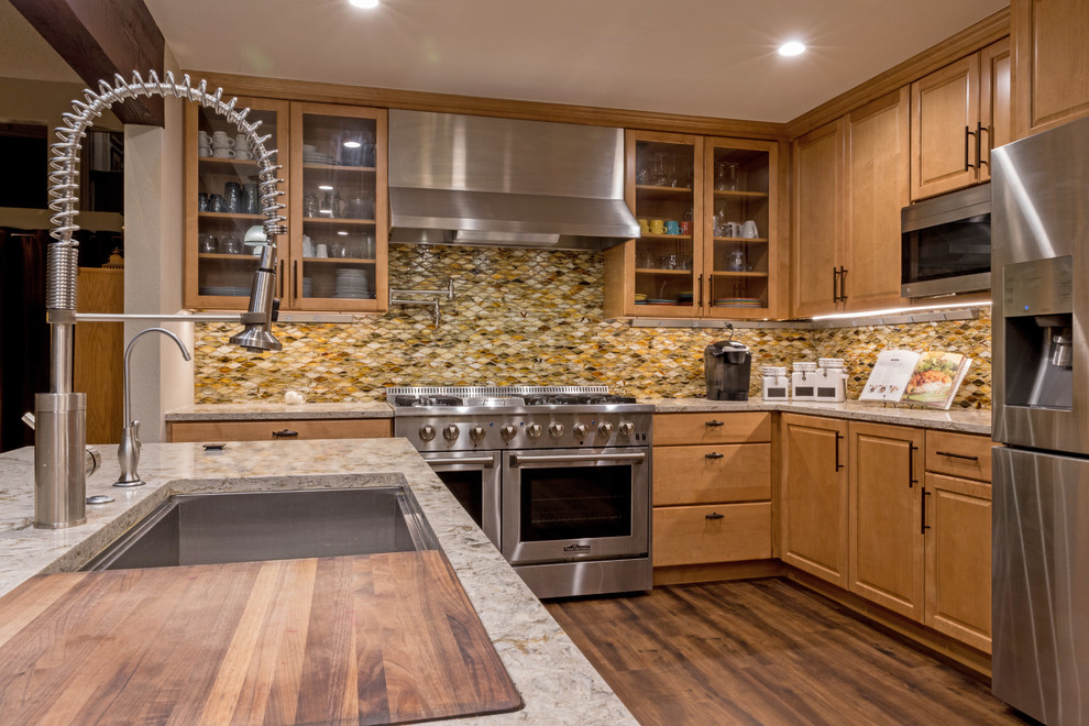 This is an example of a mid-sized transitional l-shaped eat-in kitchen in Orange County with an undermount sink, raised-panel cabinets, medium wood cabinets, quartz benchtops, brown splashback, glass tile splashback, stainless steel appliances, vinyl floors, with island, brown floor and multi-coloured benchtop.