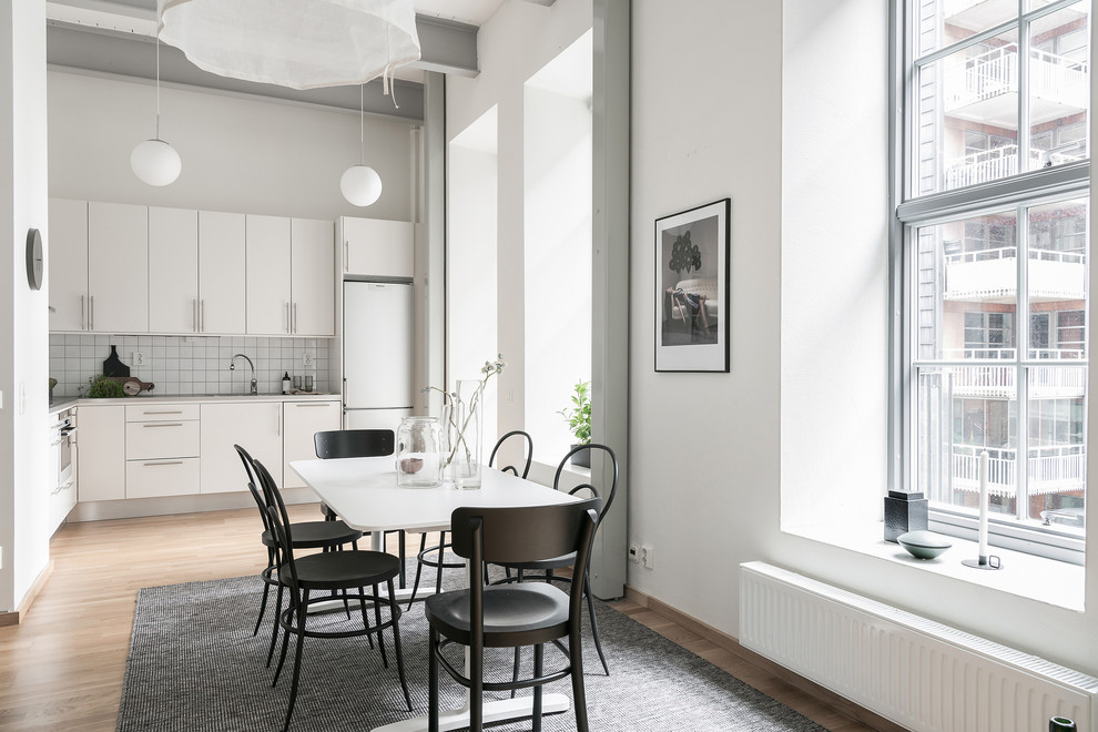 This is an example of a large scandinavian l-shaped eat-in kitchen in Gothenburg with flat-panel cabinets, white cabinets, white appliances, medium hardwood floors, no island and beige floor.