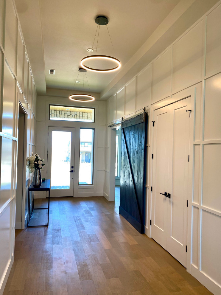 Großes Country Foyer mit weißer Wandfarbe, hellem Holzboden, Einzeltür, weißer Haustür, beigem Boden, Kassettendecke und vertäfelten Wänden in Sonstige