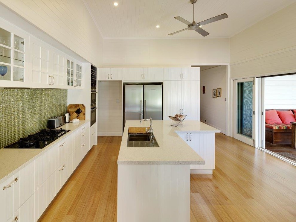 Traditional l-shaped kitchen in Gold Coast - Tweed with an undermount sink, beaded inset cabinets, white cabinets, green splashback, glass tile splashback, stainless steel appliances, light hardwood floors and with island.