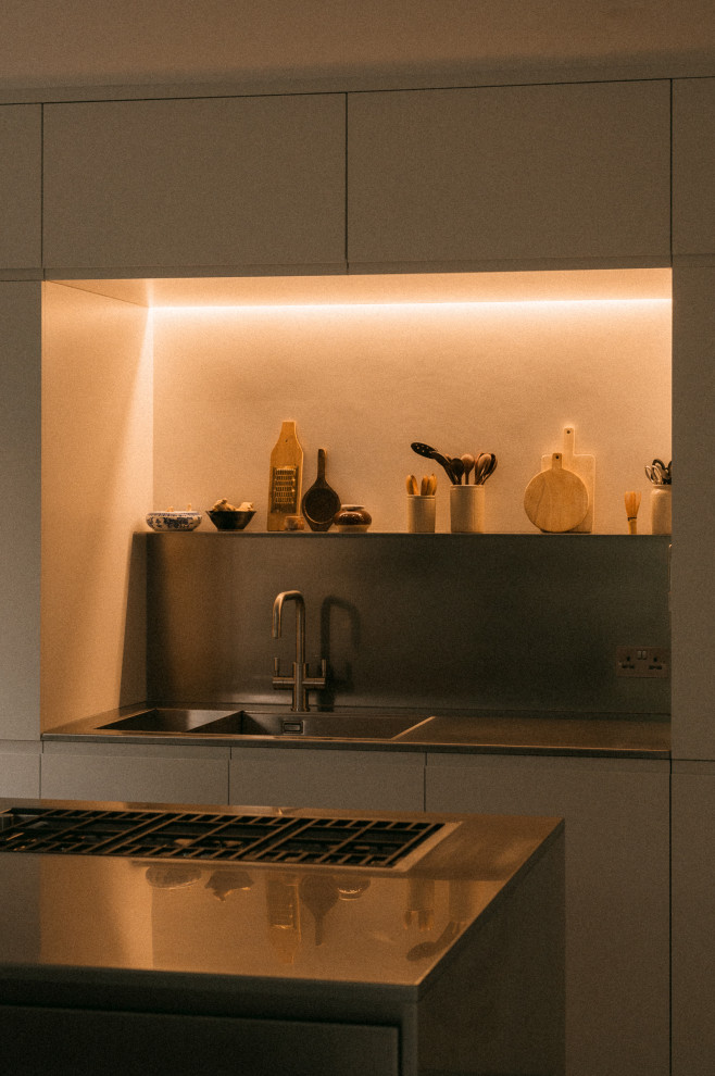 This is an example of a medium sized contemporary single-wall kitchen/diner in London with an integrated sink, flat-panel cabinets, stainless steel cabinets, stainless steel worktops, integrated appliances, concrete flooring and an island.