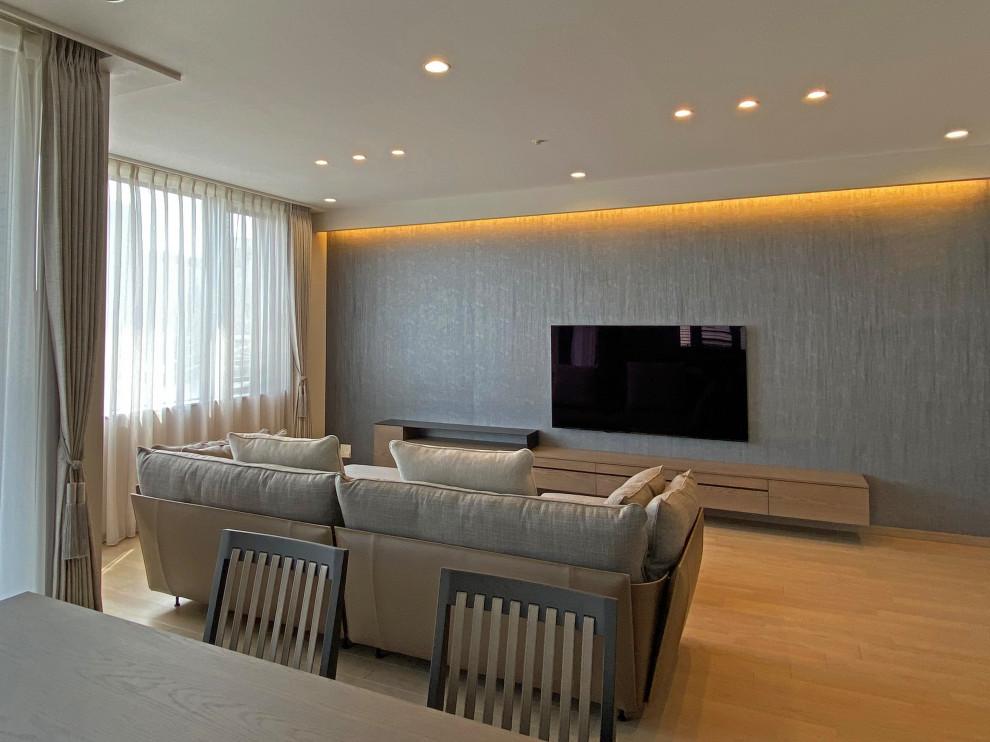 На фото: большая открытая гостиная комната с серыми стенами, деревянным полом, телевизором на стене, серым полом, потолком с обоями и обоями на стенах с