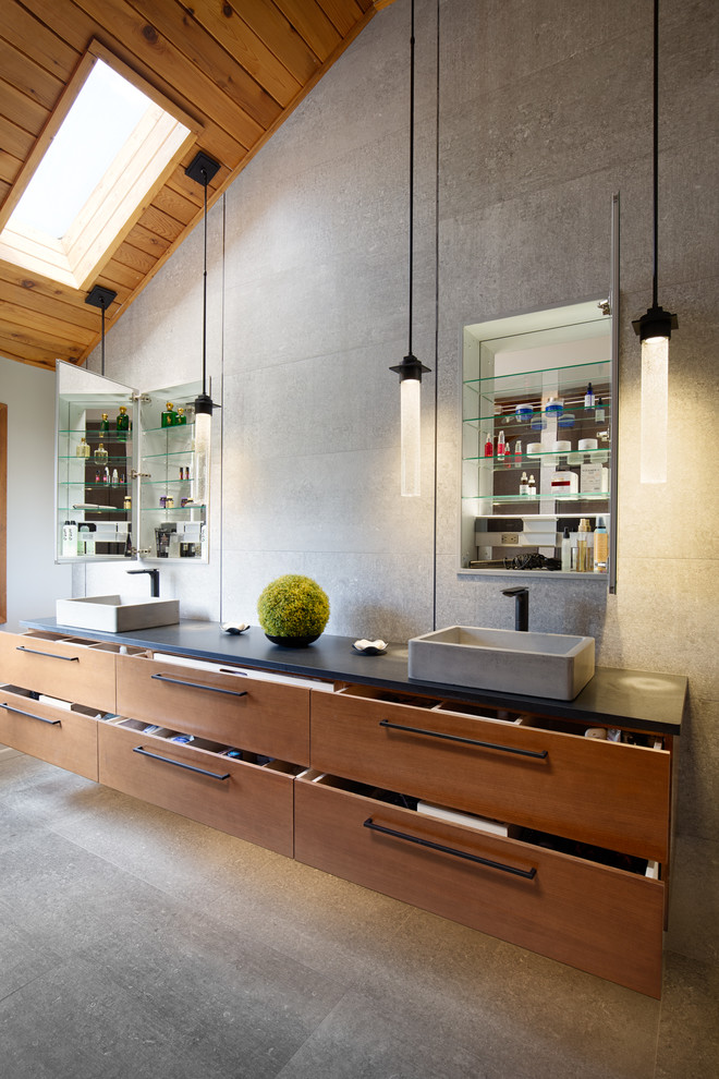 This is an example of a large contemporary master bathroom in Other with flat-panel cabinets, medium wood cabinets, a double shower, a one-piece toilet, gray tile, grey walls, a vessel sink, grey floor, a hinged shower door, black benchtops, concrete floors and concrete benchtops.