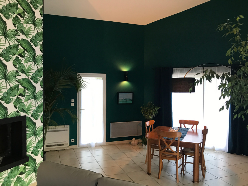 Photo of a mid-sized tropical open plan dining in Toulouse with green walls, ceramic floors, beige floor and a hanging fireplace.