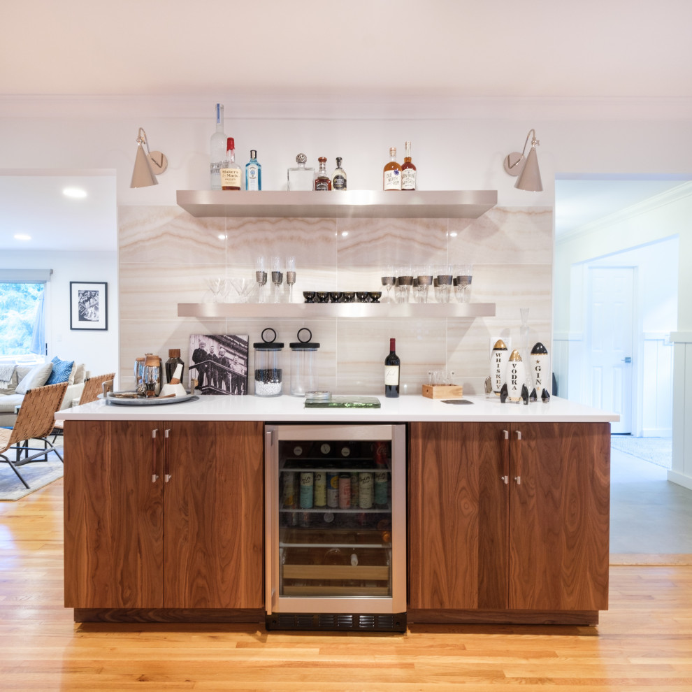 This is an example of a medium sized contemporary u-shaped kitchen pantry in New York with a belfast sink, engineered stone countertops, porcelain splashback, stainless steel appliances, an island, white worktops, flat-panel cabinets, medium wood cabinets, beige splashback, medium hardwood flooring and brown floors.