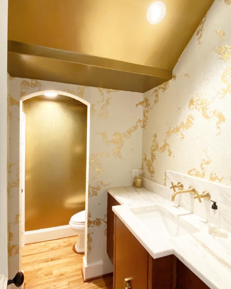 Inredning av ett klassiskt mellanstort vit vitt toalett, med släta luckor, skåp i mörkt trä, en toalettstol med separat cisternkåpa, mörkt trägolv, ett undermonterad handfat, marmorbänkskiva och brunt golv