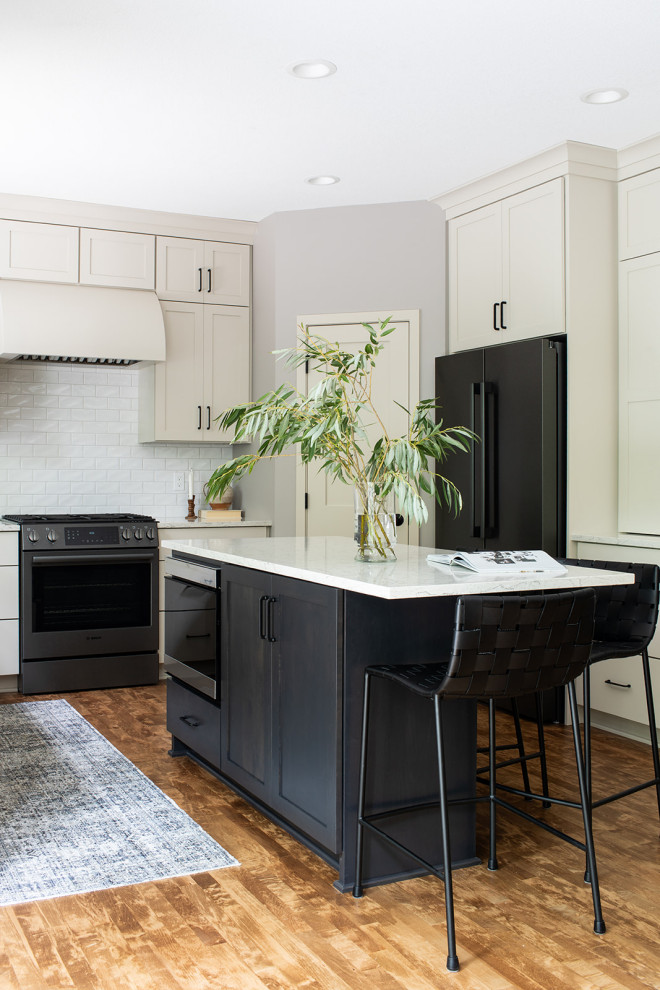 Example of a mid-sized transitional u-shaped medium tone wood floor and brown floor eat-in kitchen design with an undermount sink, shaker cabinets, white cabinets, quartz countertops, white backsplash, subway tile backsplash, black appliances, an island and white countertops