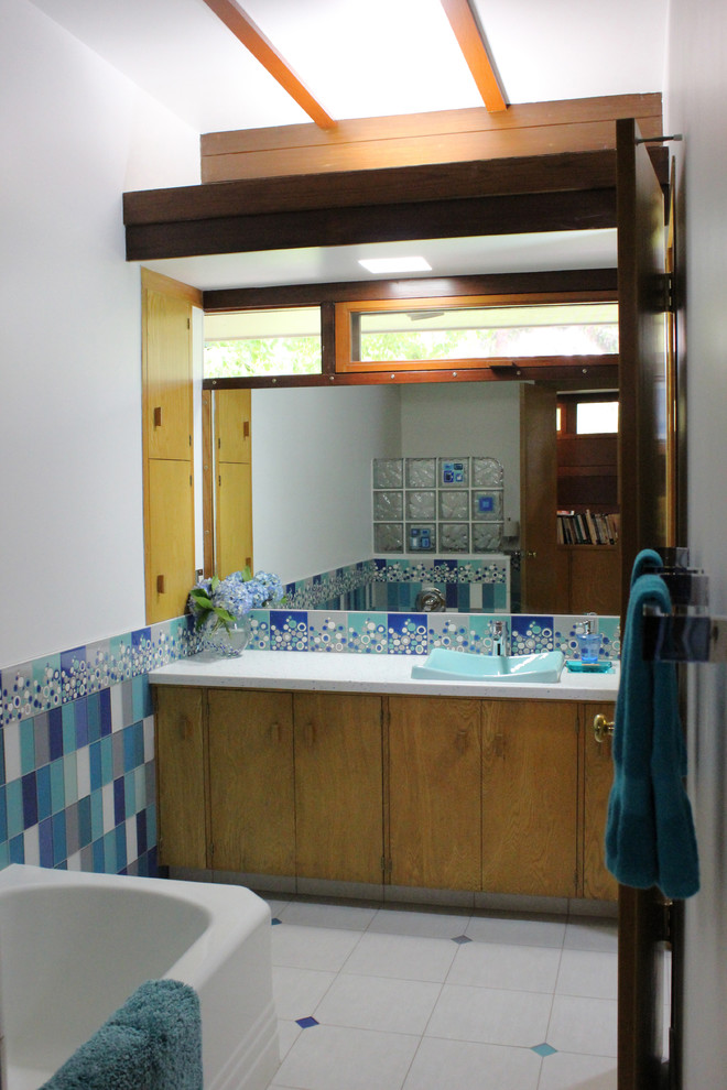 Mid-sized modern kids bathroom in San Francisco with flat-panel cabinets, medium wood cabinets, solid surface benchtops, a freestanding tub, blue tile, glass tile, blue walls and ceramic floors.