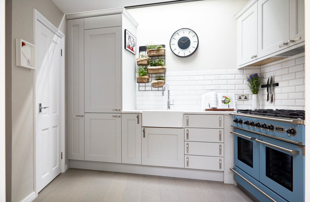Inspiration for a small transitional l-shaped separate kitchen in London with a farmhouse sink, shaker cabinets, grey cabinets, quartzite benchtops, white splashback, porcelain splashback, coloured appliances, light hardwood floors, no island, grey floor and white benchtop.