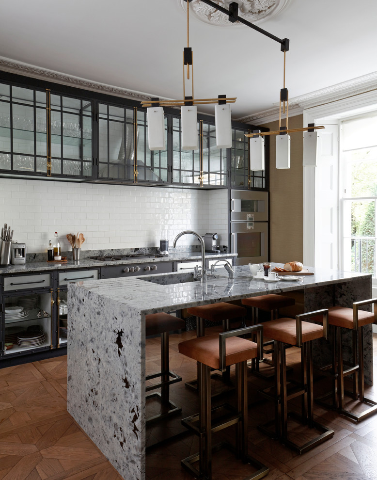 Photo of a mid-sized midcentury single-wall open plan kitchen in London with a drop-in sink, glass-front cabinets, black cabinets, marble benchtops, grey splashback, marble splashback, panelled appliances, medium hardwood floors, with island, brown floor and grey benchtop.