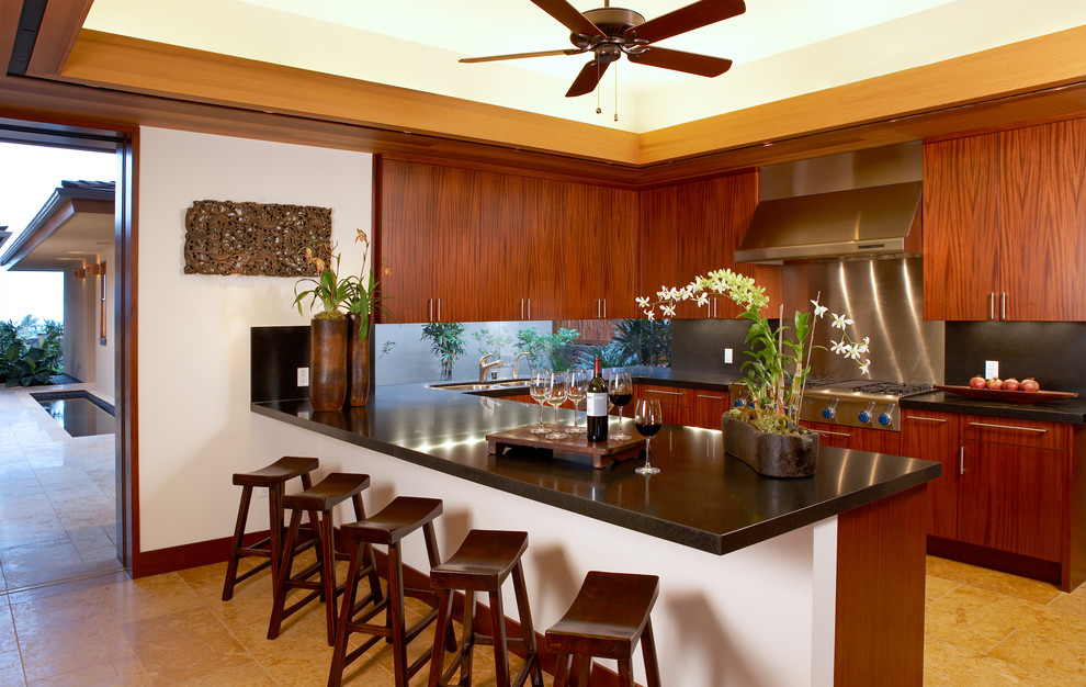 Photo of a tropical u-shaped kitchen in Hawaii with an undermount sink, flat-panel cabinets, dark wood cabinets and black splashback.