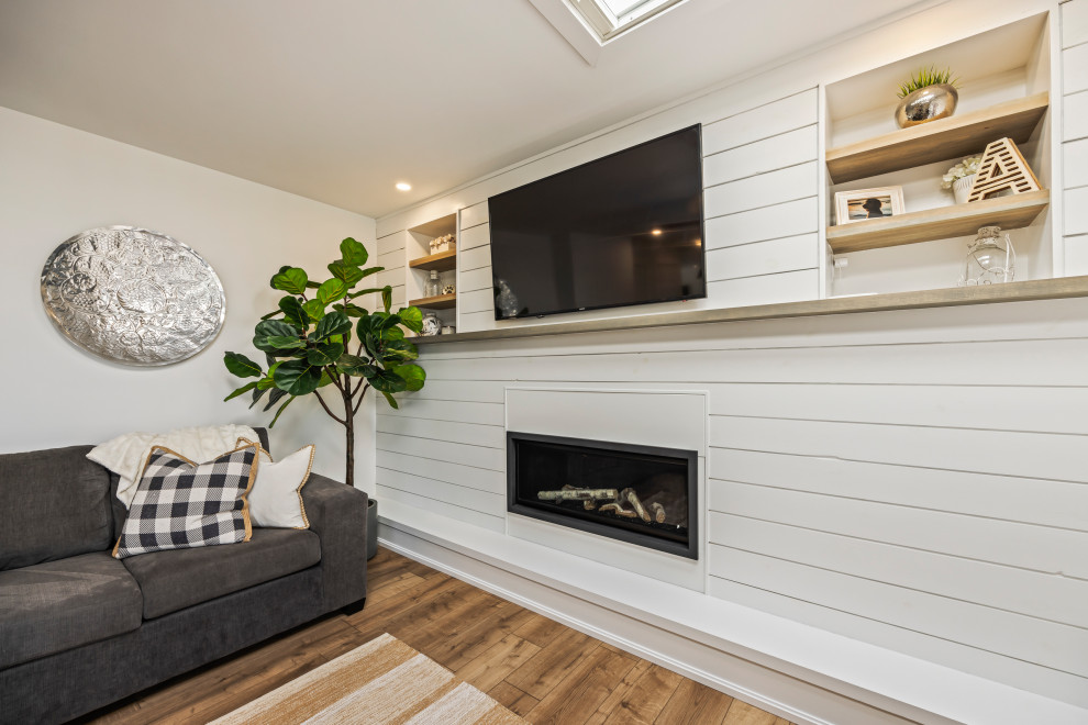 Mittelgroßes, Abgetrenntes Modernes Wohnzimmer mit weißer Wandfarbe, Kamin, Kaminumrandung aus Holzdielen, TV-Wand und braunem Boden in Toronto