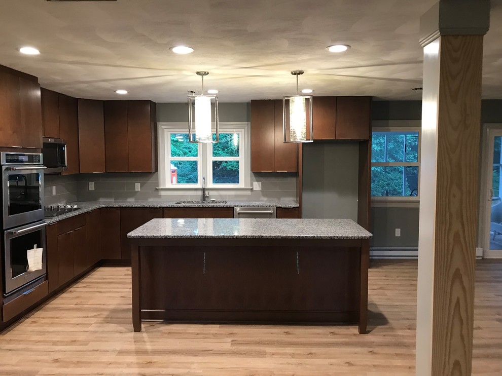 Inspiration for a mid-sized transitional l-shaped light wood floor and beige floor open concept kitchen remodel with a drop-in sink, flat-panel cabinets, brown cabinets, granite countertops, gray backsplash, mosaic tile backsplash, stainless steel appliances, an island and gray countertops