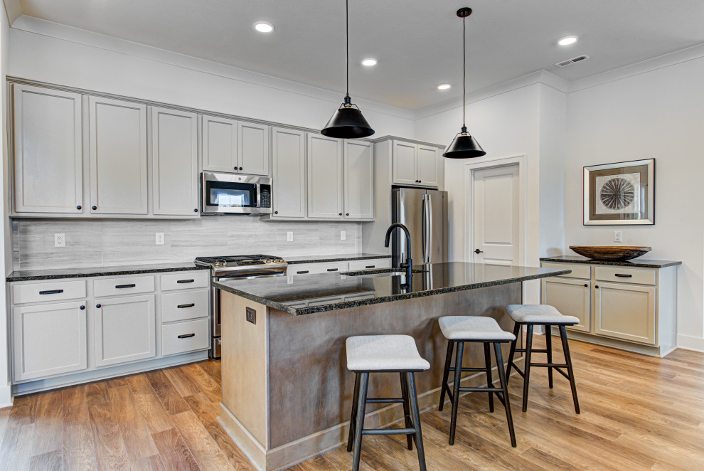 Foto på ett mellanstort amerikanskt svart kök, med grått stänkskydd, rostfria vitvaror, vinylgolv, en köksö, brunt golv, en undermonterad diskho, skåp i shakerstil, beige skåp, granitbänkskiva och stänkskydd i keramik