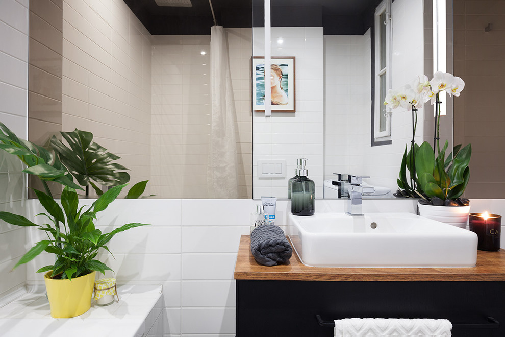 This is an example of a small contemporary master bathroom in Other with furniture-like cabinets, black cabinets, a drop-in tub, a shower/bathtub combo, a wall-mount toilet, black and white tile, ceramic tile, white walls, ceramic floors, a vessel sink, black floor and a shower curtain.