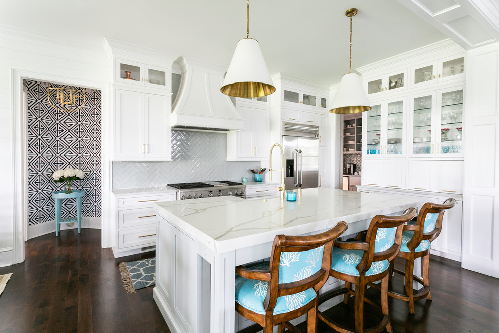 Photo of a beach style kitchen in Charleston with a farmhouse sink, glass-front cabinets, white cabinets, grey splashback, stainless steel appliances, dark hardwood floors, with island and white benchtop.