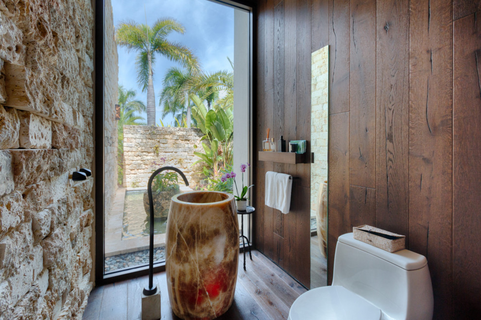 Ispirazione per una stanza da bagno tropicale con piastrelle beige, parquet scuro, lavabo a colonna, pavimento marrone, un lavabo e pareti in legno