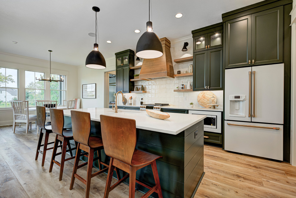 Mid-sized transitional galley vinyl floor and brown floor eat-in kitchen photo in Indianapolis with a farmhouse sink, shaker cabinets, green cabinets, granite countertops, white backsplash, ceramic backsplash, white appliances, an island and white countertops