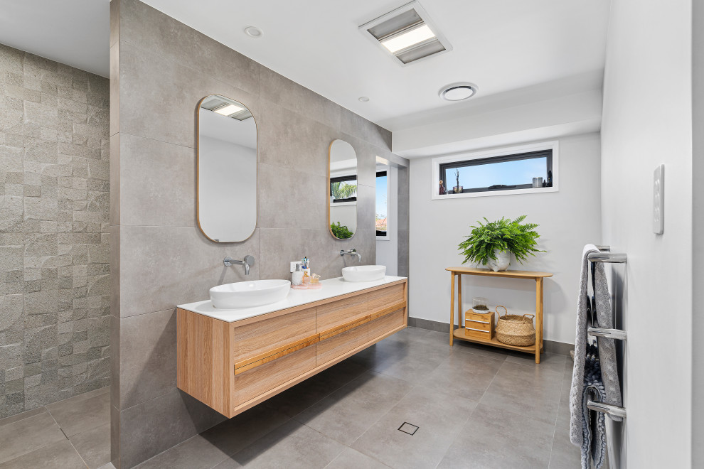 Photo of a large contemporary master bathroom in Gold Coast - Tweed with flat-panel cabinets, light wood cabinets, an alcove shower, gray tile, porcelain tile, grey walls, porcelain floors, a vessel sink, solid surface benchtops, grey floor, an open shower and white benchtops.
