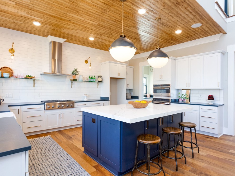 Design ideas for a mid-sized country u-shaped open plan kitchen in Other with a farmhouse sink, shaker cabinets, white cabinets, white splashback, subway tile splashback, medium hardwood floors, with island, brown floor and black benchtop.