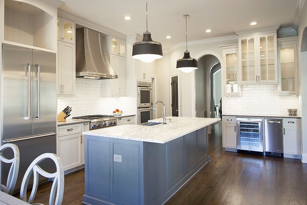 Photo of a large transitional u-shaped eat-in kitchen in Charlotte with a farmhouse sink, flat-panel cabinets, white cabinets, marble benchtops, white splashback, ceramic splashback, stainless steel appliances, medium hardwood floors and with island.