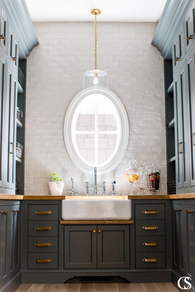 This is an example of a mid-sized transitional u-shaped kitchen pantry in Salt Lake City with a farmhouse sink, shaker cabinets, black cabinets, wood benchtops, white splashback, subway tile splashback and light hardwood floors.