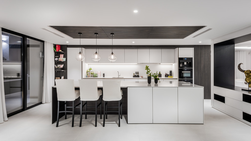 This is an example of a contemporary galley kitchen in Other with an undermount sink, flat-panel cabinets, white cabinets, black appliances, with island, grey floor and white benchtop.