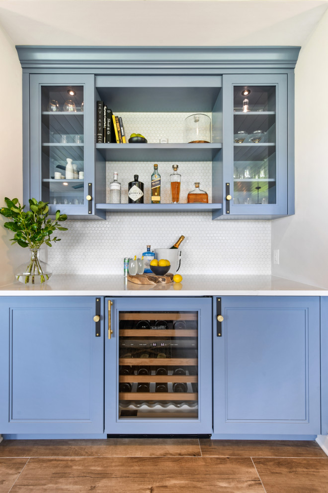 Design ideas for a mid-sized beach style l-shaped home bar in Other with shaker cabinets, blue cabinets, quartz benchtops, white splashback, porcelain splashback, porcelain floors, brown floor and white benchtop.