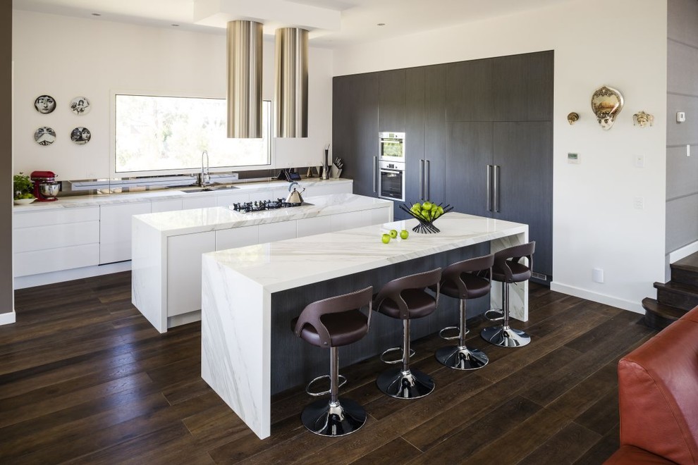 Inspiration for a contemporary galley open plan kitchen in Melbourne with flat-panel cabinets, dark wood cabinets, white splashback, stainless steel appliances, dark hardwood floors, multiple islands, an undermount sink, marble benchtops and mirror splashback.