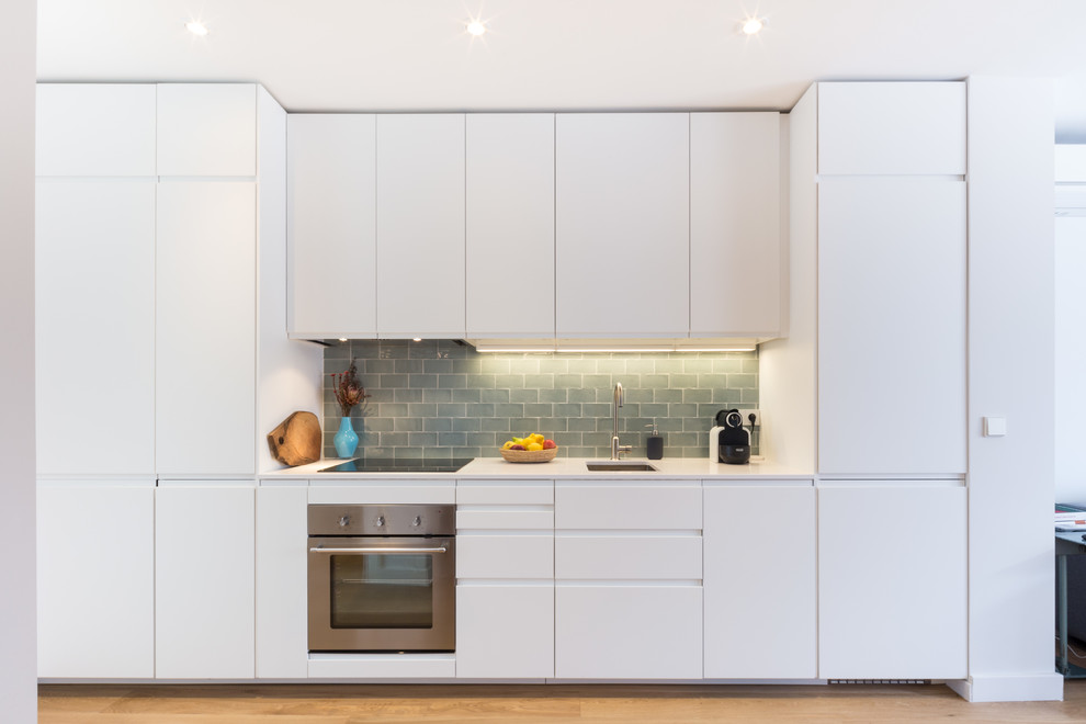 Design ideas for a small contemporary single-wall open plan kitchen in Madrid with an undermount sink, flat-panel cabinets, white cabinets, quartz benchtops, green splashback, ceramic splashback, stainless steel appliances, no island, medium hardwood floors and brown floor.