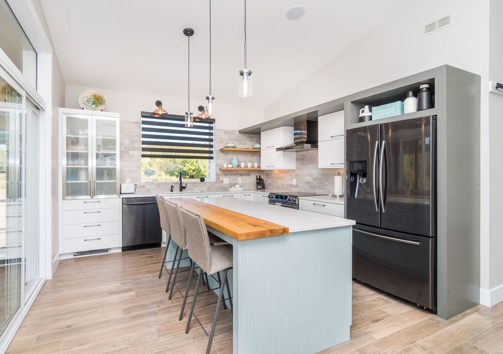 Example of a large transitional l-shaped light wood floor and brown floor kitchen design with an undermount sink, flat-panel cabinets, white cabinets, quartz countertops, brown backsplash, subway tile backsplash, stainless steel appliances and an island