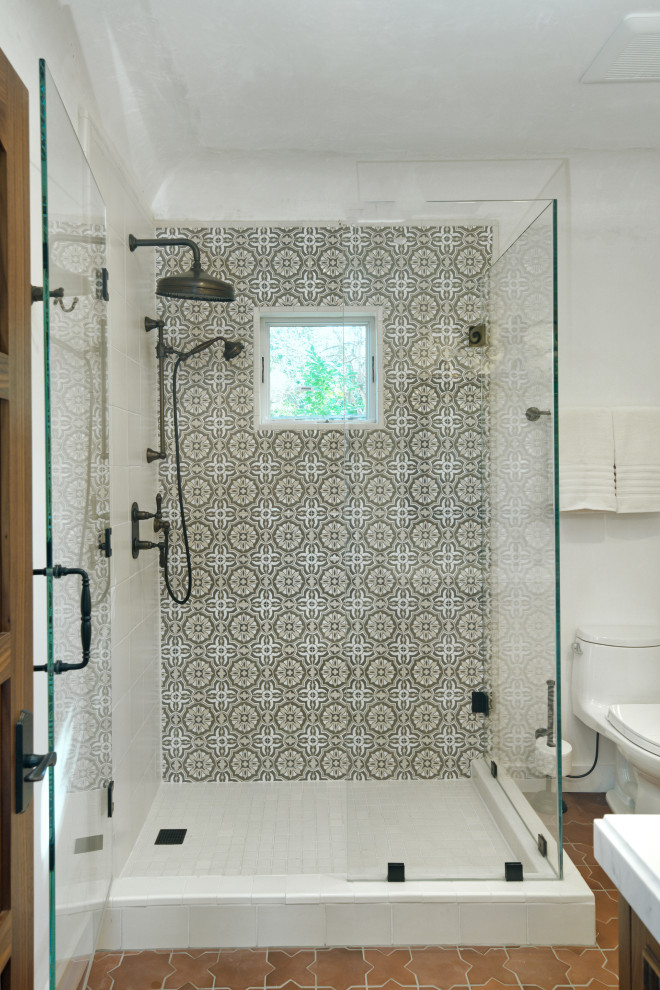 Photo of a mid-sized mediterranean bathroom in San Francisco with a corner shower, a one-piece toilet, ceramic tile, white walls, porcelain floors, red floor and a hinged shower door.