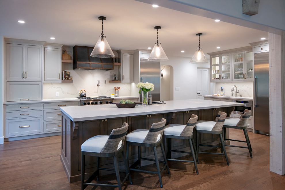 Open concept kitchen - huge transitional l-shaped medium tone wood floor and brown floor open concept kitchen idea with an undermount sink, shaker cabinets, gray cabinets, quartz countertops, white backsplash, quartz backsplash, stainless steel appliances, an island and white countertops