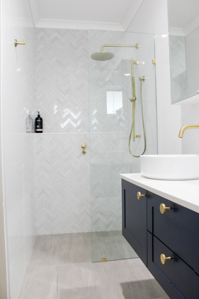 This is an example of a mid-sized contemporary master bathroom in Perth with shaker cabinets, blue cabinets, an open shower, a one-piece toilet, white tile, ceramic tile, white walls, porcelain floors, a vessel sink, engineered quartz benchtops, grey floor, an open shower and white benchtops.
