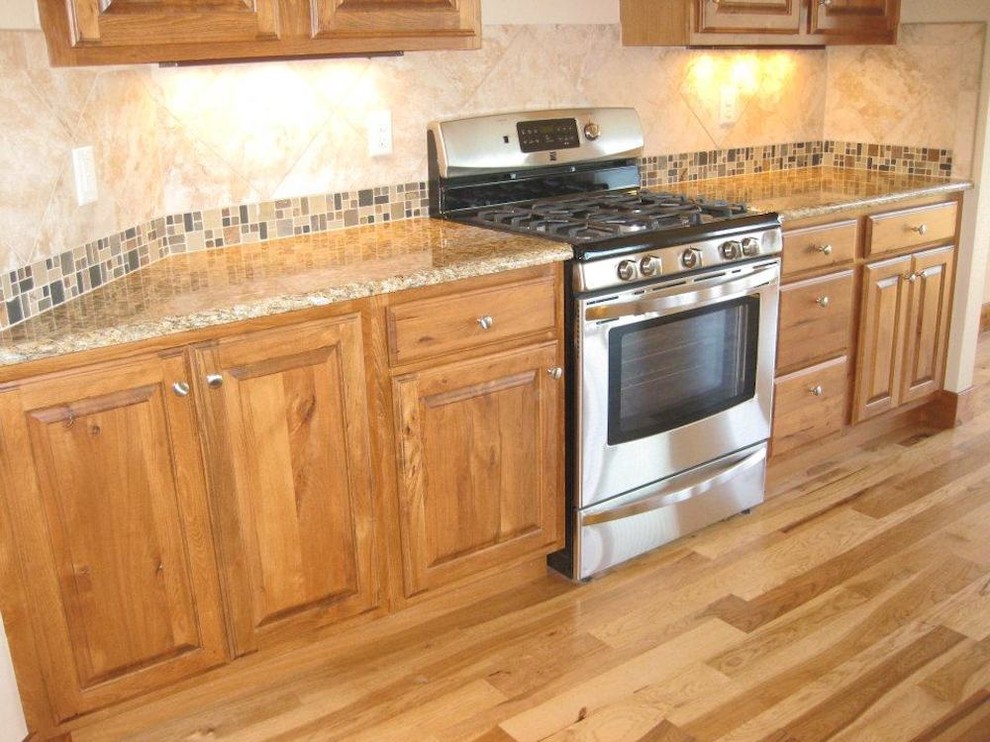Mid-sized mountain style galley medium tone wood floor open concept kitchen photo with raised-panel cabinets, medium tone wood cabinets, granite countertops, multicolored backsplash, ceramic backsplash, stainless steel appliances, a double-bowl sink and a peninsula