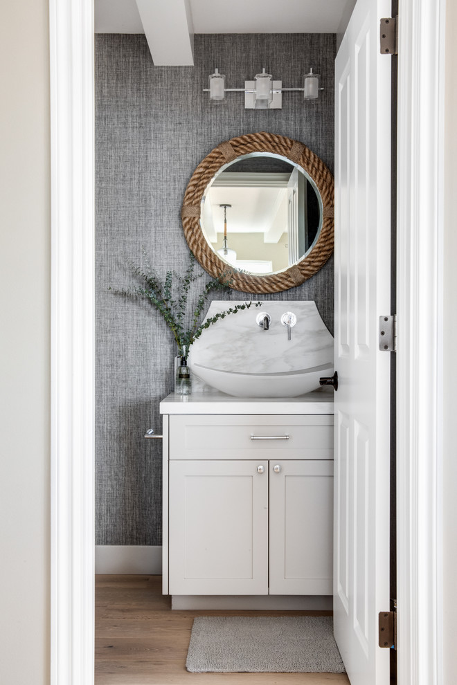 Photo of a small beach style powder room in Los Angeles with grey cabinets, light hardwood floors, a vessel sink, shaker cabinets, grey walls, beige floor and white benchtops.