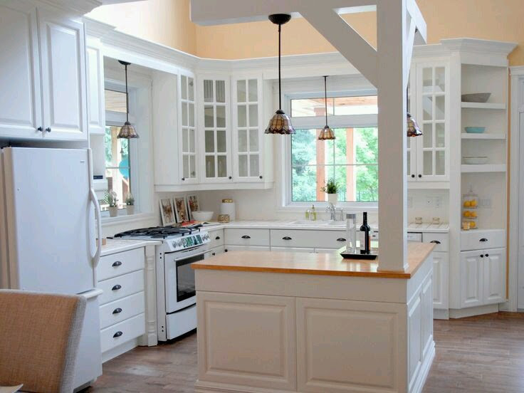 This is an example of a mid-sized country l-shaped eat-in kitchen in Montreal with a double-bowl sink, glass-front cabinets, white cabinets, wood benchtops, white appliances, medium hardwood floors, with island, brown floor, white benchtop and white splashback.
