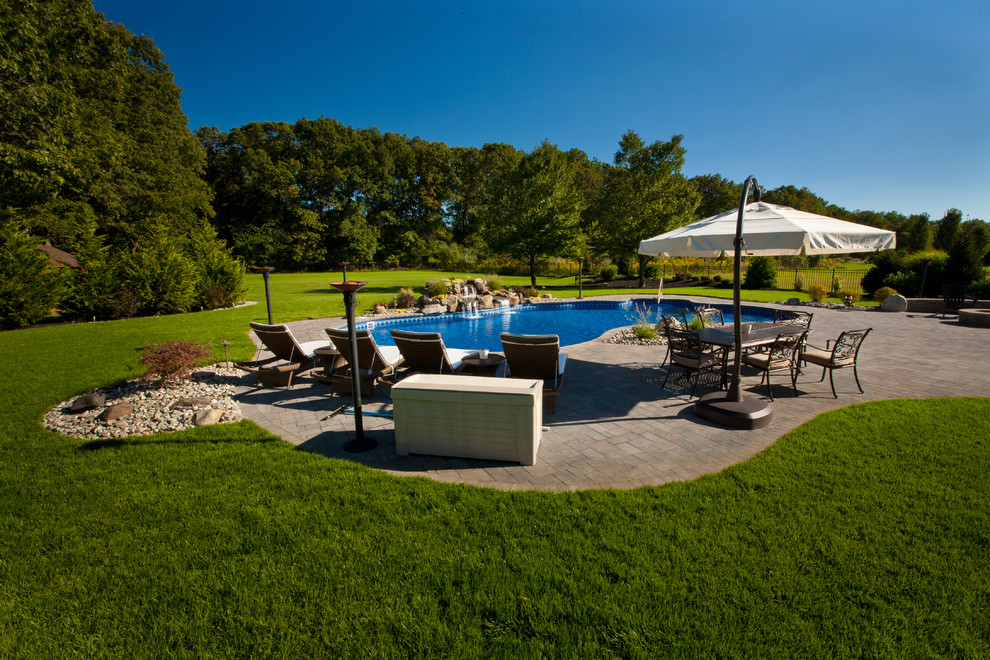 This is an example of a large modern backyard custom-shaped lap pool in Philadelphia with a water feature and natural stone pavers.