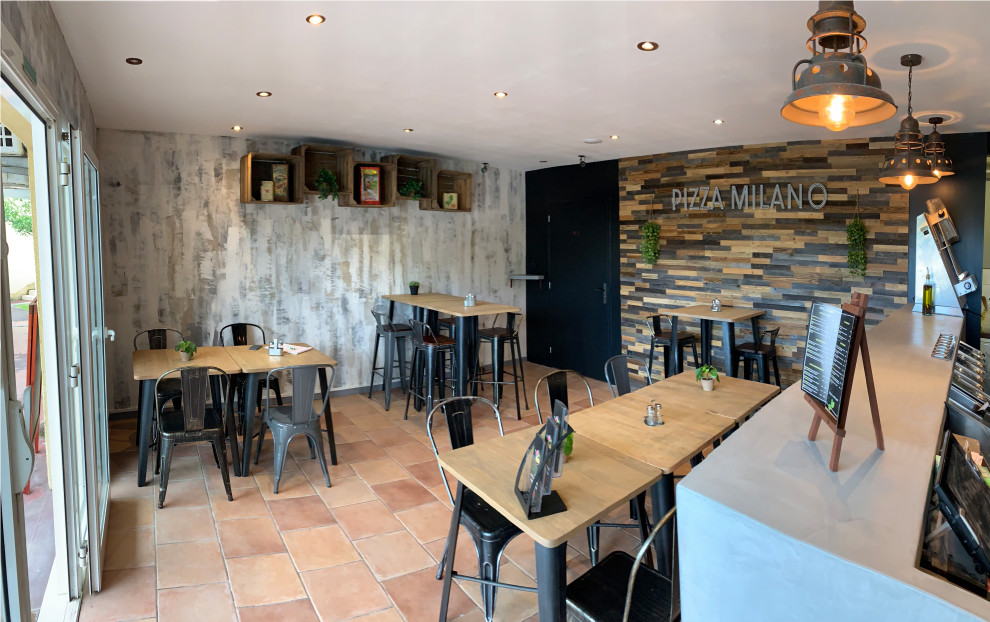 This is an example of a mid-sized industrial open plan dining in Bordeaux with grey walls, terra-cotta floors and wood walls.