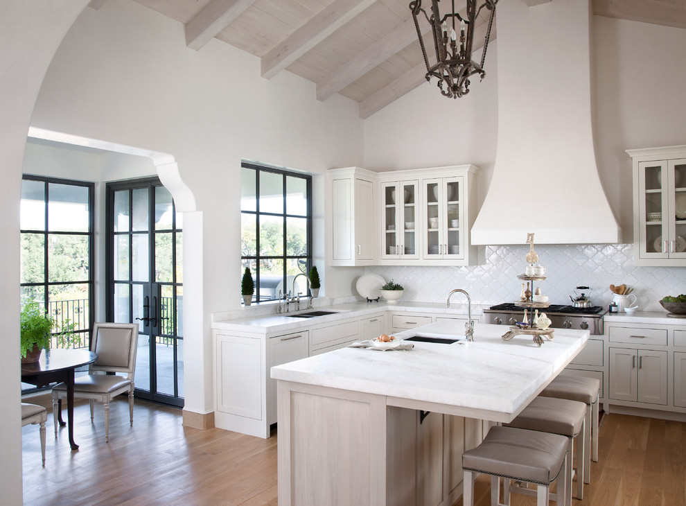 Inspiration for a mediterranean medium tone wood floor eat-in kitchen remodel in Austin with shaker cabinets, white cabinets, white backsplash and an island