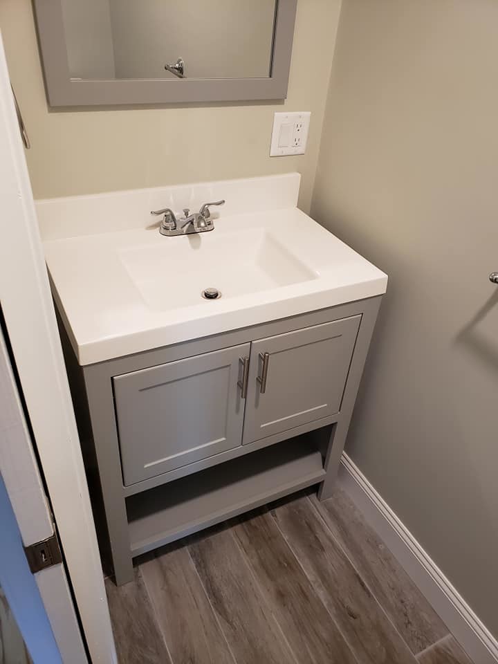 Inspiration for a small contemporary 3/4 bathroom in Boston with raised-panel cabinets, grey cabinets, a two-piece toilet, gray tile, porcelain tile, grey walls, porcelain floors, an integrated sink, solid surface benchtops, brown floor and white benchtops.