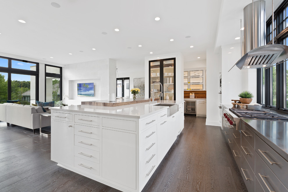 This is an example of a large contemporary u-shaped eat-in kitchen in Minneapolis with a farmhouse sink, flat-panel cabinets, white cabinets, wood benchtops, stainless steel appliances, medium hardwood floors, with island, brown floor and brown benchtop.